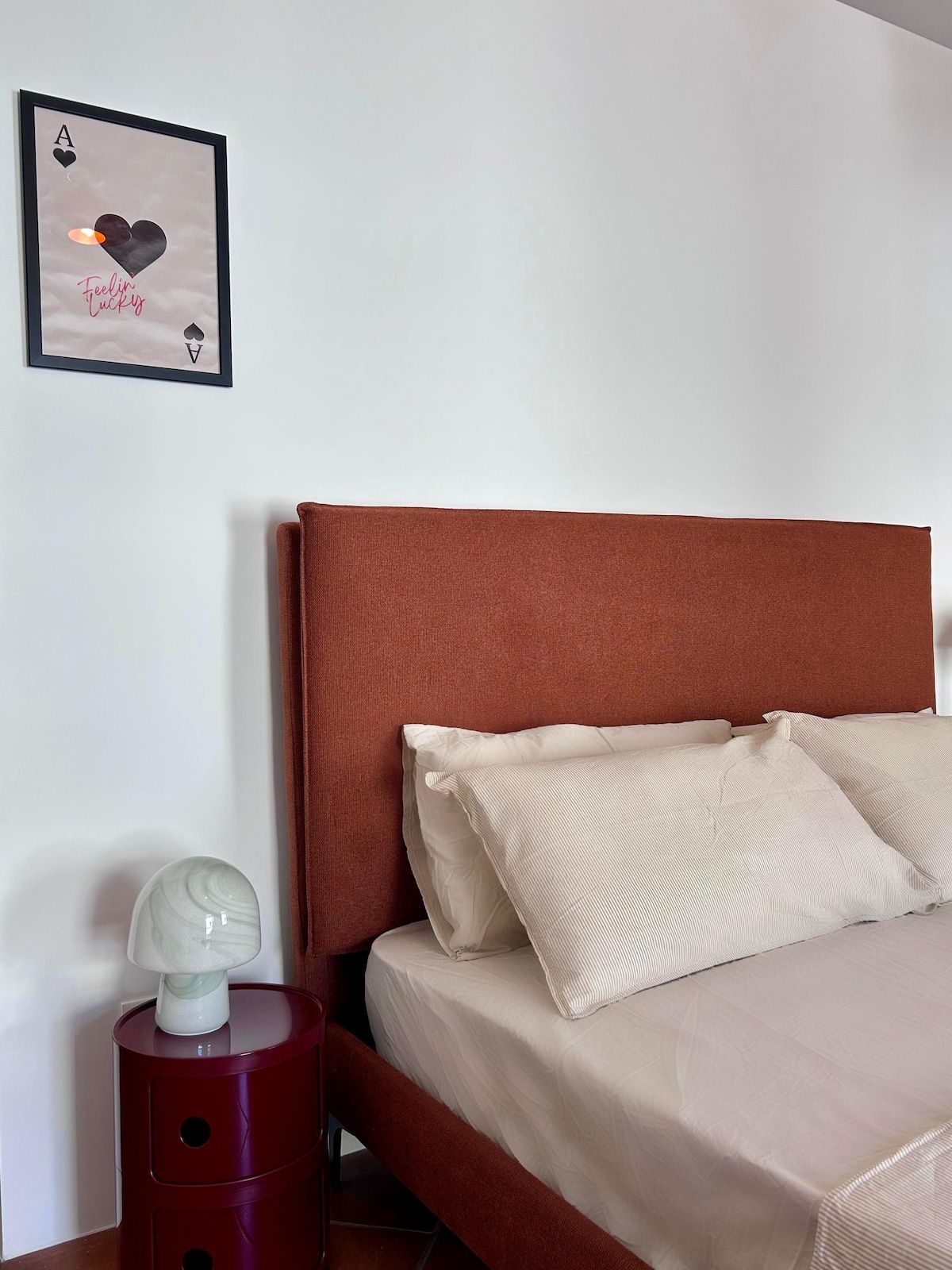 A bedroom with a bed, pillows, a nightstand, a framed picture, and a lamp.