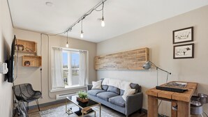 Ein modernes Wohnzimmer mit einem grauen Sofa, einem Holztisch, einem schwarzen Sessel, einer Stehlampe und einem an der Wand befestigten Regal.
