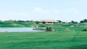 Ein Golfplatz mit Teich, einem Gebäude im Hintergrund und sanften, grünen Hügeln.