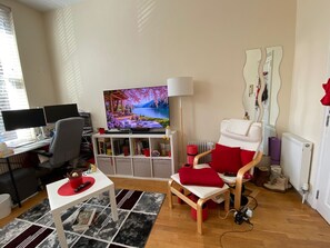 Ein modernes Wohnzimmer mit Fernseher, Schreibtisch und bequemen Sitzgelegenheiten.