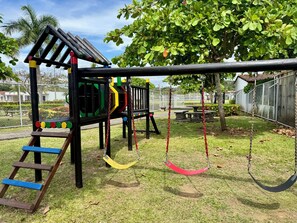 A playground with a climbing structure, swings, and a slide. - Beachfront Top Floor + Balcony | Teak Design (Bejuco)