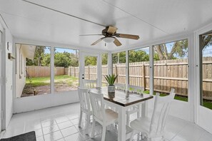 Eine überdachte Terrasse mit Deckenventilator, weißen Stühlen und einem Tisch mit einer Topfpflanze.