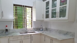 Une cuisine avec des meubles blancs, un plan de travail en marbre, une fenêtre ornée d’une grille métallique et un panier rouge.