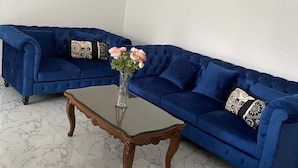 Une pièce avec un canapé bleu, une table basse en verre et un vase rempli de fleurs.