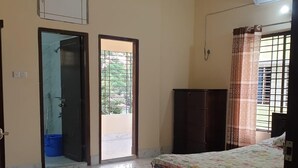 Une chambre à coucher comprenant un lit, une armoire, un ventilateur de plafond, une fenêtre avec des rideaux et une porte donnant sur un balcon.