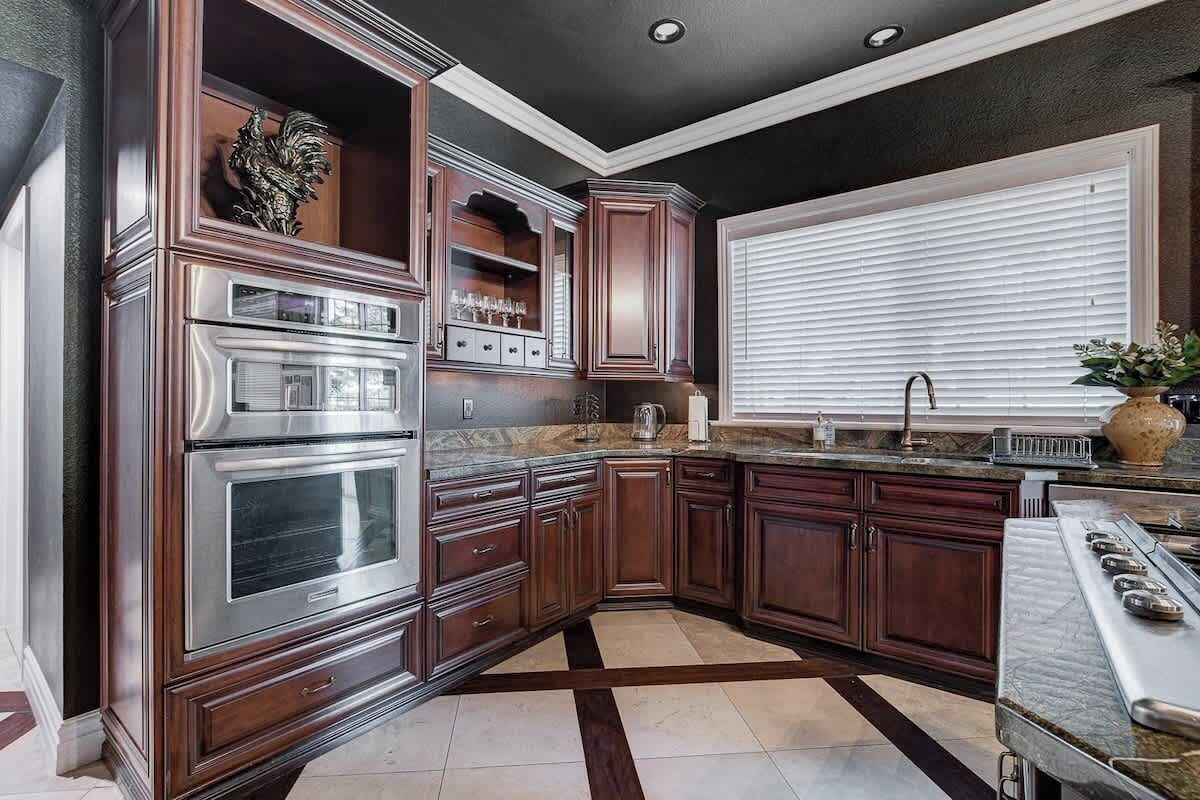 A kitchen with dark wood cabinets, stainless steel appliances, and a window with blinds.