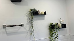 A bathroom with white walls, a towel rack, and three black shelves with plants and decorative items. - Salvation View 2 Bed Apartment (Benfleet)