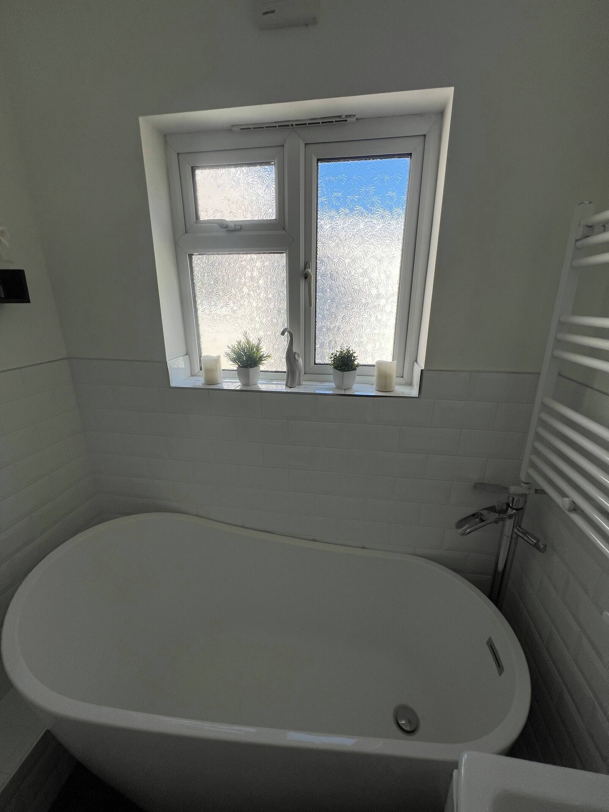Een badkamer met een vrijstaand bad, een raam met gezandstraald glas en een handdoekhouder.