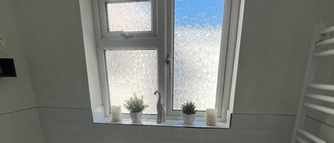 Een badkamer met een vrijstaand bad, een raam met gezandstraald glas en een handdoekhouder.