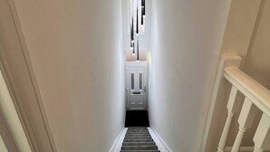A staircase with a white railing, carpeted steps, and a modern light fixture at the top. - Salvation View 2 Bed Apartment (Benfleet)
