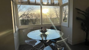 A corner room with a bay window, a round glass table, and a chair. - Salvation View 2 Bed Apartment (Benfleet)