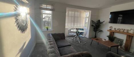 Ein Wohnzimmer mit Sofa, einem Esstisch mit Stühlen, einem an der Wand befestigten Fernseher und einem Kamin.