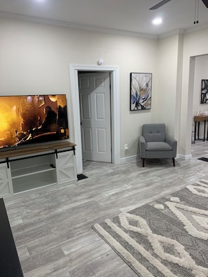 A living room with a flat-screen TV, a gray armchair, a wooden coffee table, and a patterned rug.