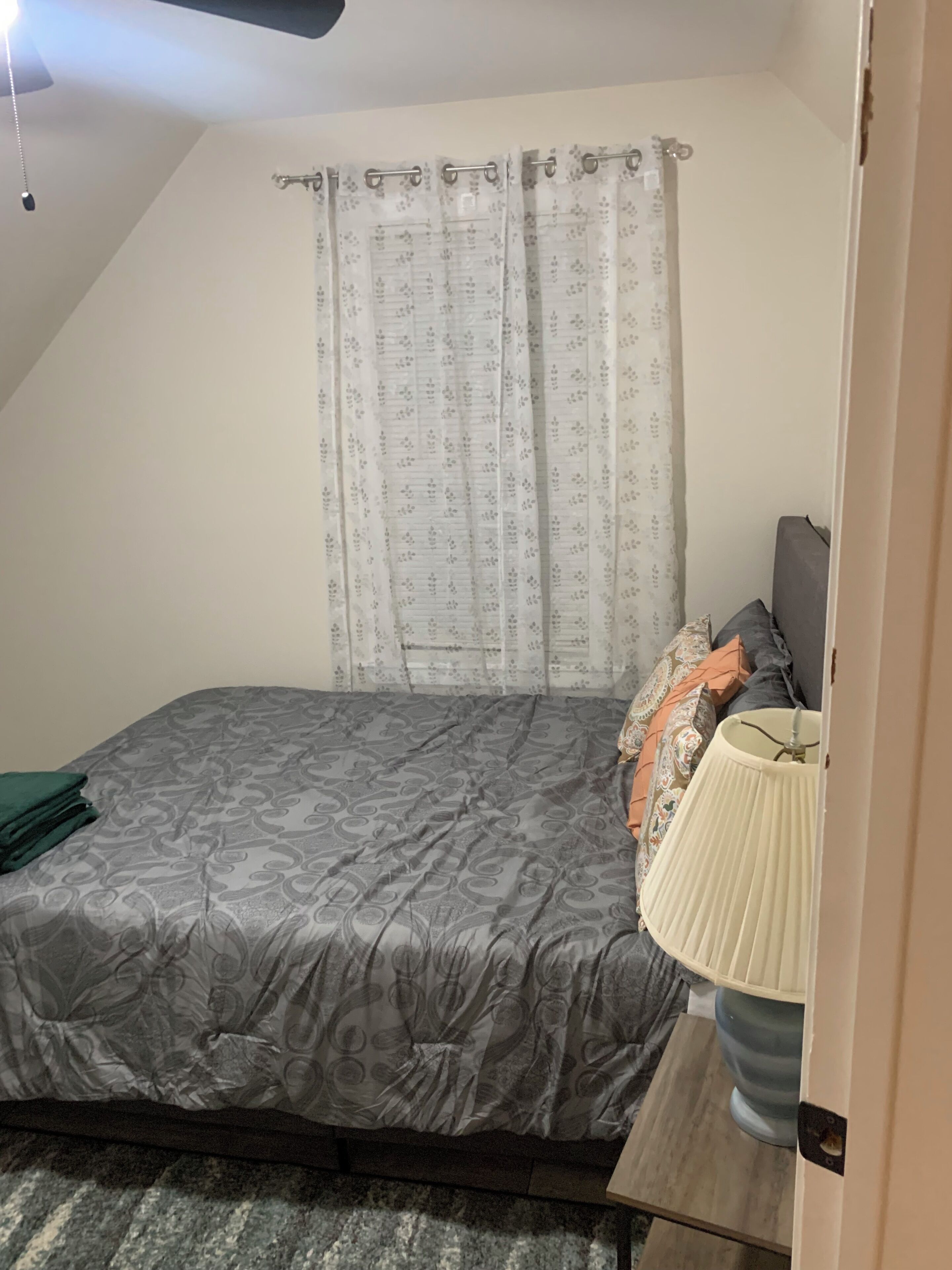 Une chambre à coucher avec un lit, une lampe de chevet, une fenêtre avec des rideaux et un ventilateur de plafond.