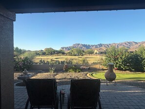A patio with two chairs, a large vase, and a view of a vineyard and mountains.