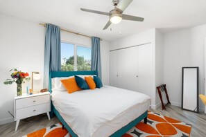 A bedroom with a bed, a nightstand, a desk, a ceiling fan, and a window with curtains. - Mid-Century 3BR Near Banner & ASU | Extended Stay (Tempe)