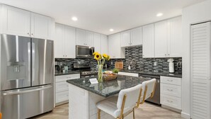 A modern kitchen with white cabinets, stainless steel appliances, a granite countertop, and a central island with bar stools. - Mid-Century 3BR Near Banner & ASU | Extended Stay (Tempe)