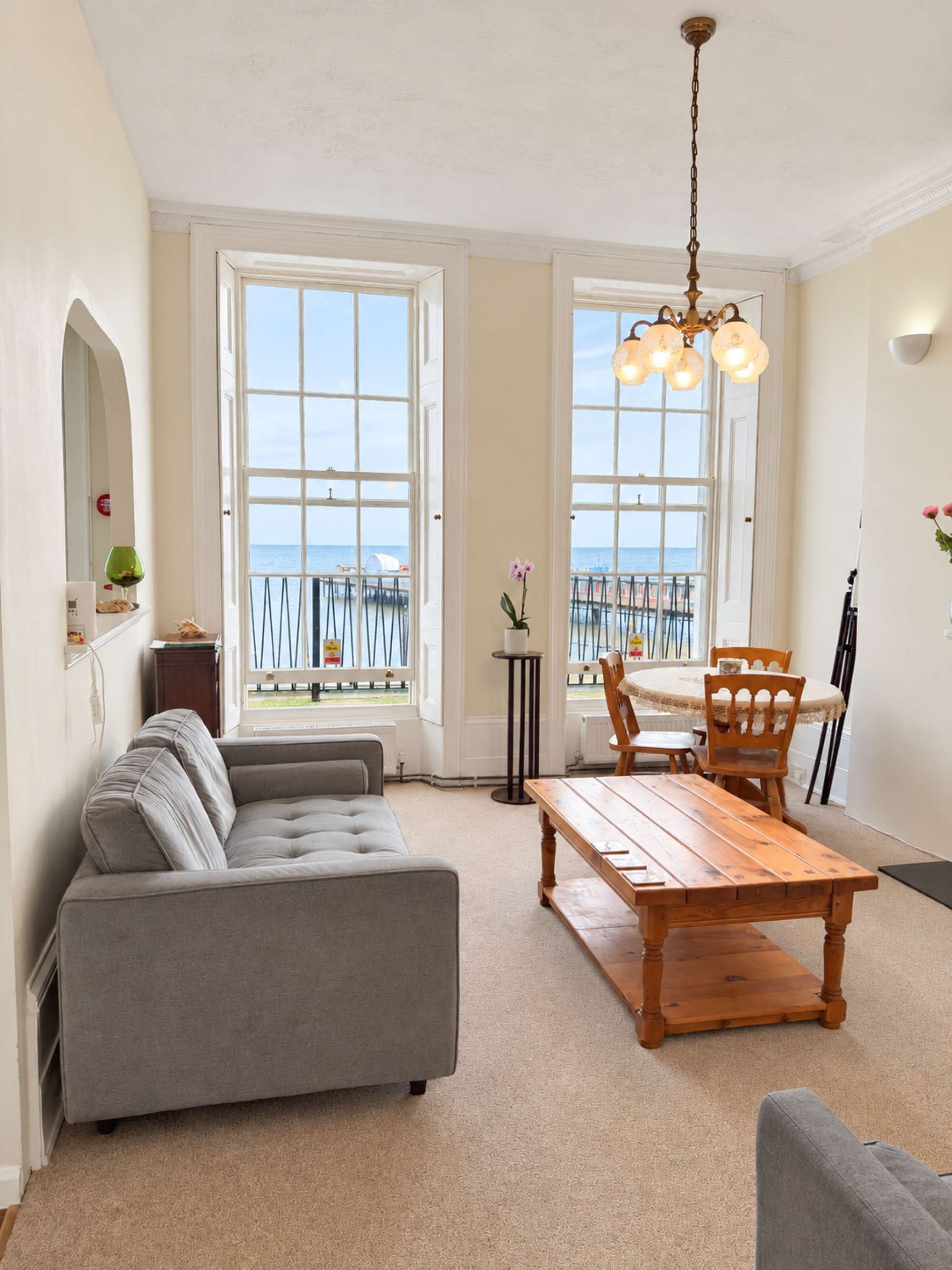 Ein Wohnzimmer mit Sofa, Esstisch, Stühlen und Meerblick durch große Fenster.