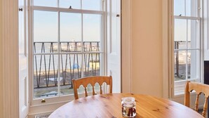 Quarto com uma grande janela com vista para a frente do mar, uma mesa de madeira e uma cadeira.