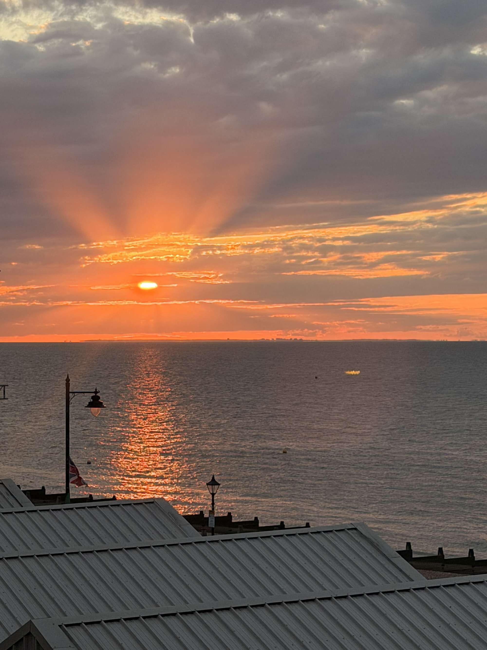 A sunset over the ocean with a view of the sea and a building with a metal roof.