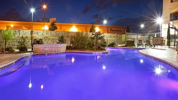 A swimming pool at night with surrounding stone walls and a fence.