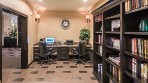 A well-lit office space with a desk, two chairs, a computer, a clock, and a bookshelf filled with books.