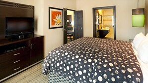 A hotel room with a bed, a TV, a desk, and a bathroom visible through an open door.