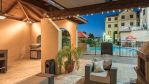 An outdoor patio area with a grill, seating, and a pool in the background.