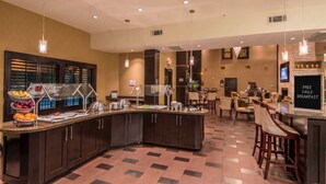 Un espace petit-déjeuner d’hôtel avec un buffet, des tables et des chaises, ainsi qu’un panneau indiquant que le petit-déjeuner est offert gratuitement chaque jour.