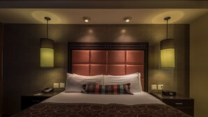 Une chambre d’hôtel avec un grand lit, deux tables de chevet, une tête de lit à motifs géométriques et deux lampes fixées au mur.