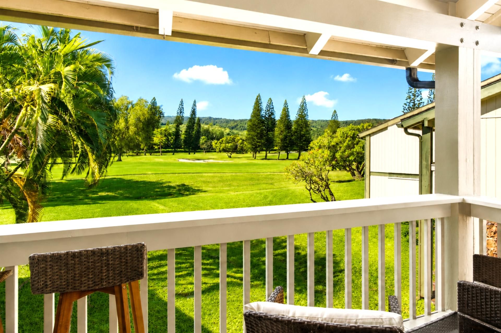 A balcony with wicker furniture overlooking a golf course with trees and a clear sky.