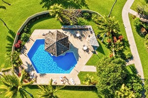 Eine Vogelperspektive auf einen Swimmingpool mit einer sechseckigen Poolterrasse, umgeben von Palmen und einem Garten.