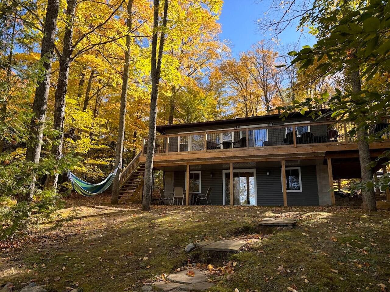 A two-story cabin with a deck, surrounded by trees with autumn foliage.