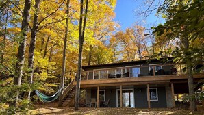 A two-story cabin with a deck, surrounded by trees with autumn foliage. - Diamond Lakehouse | SUP, Canoe, BBQ, Aurora Magic (Highland Grove)