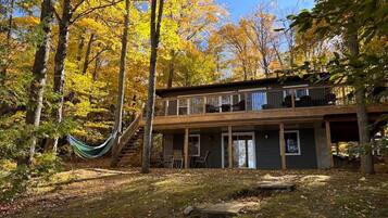 A two-story cabin with a deck, surrounded by trees with autumn foliage.