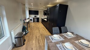 A modern kitchen with a built-in washing machine, a dining area with a table set for four, and a compact living space. - 5BR Home w/ Parking for Groups & Contractors (Portsmouth)