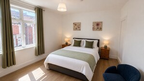 A bedroom with a bed, two bedside lamps, a chair, a window with curtains, and two wall art pieces. - 5BR Home w/ Parking for Groups & Contractors (Portsmouth)