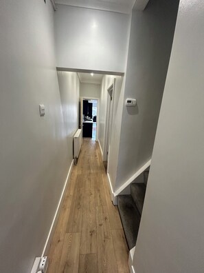Ein schmaler Korridor mit Holzdielen, weißen Wänden und einer Tür zu einer Küchenzeile.