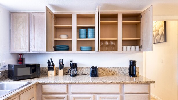A kitchen with wooden cabinets, a granite countertop, a microwave, a coffee maker, and various kitchen utensils. - Classy 70-ies style home with Mineralized Spa (Desert Hot Springs)