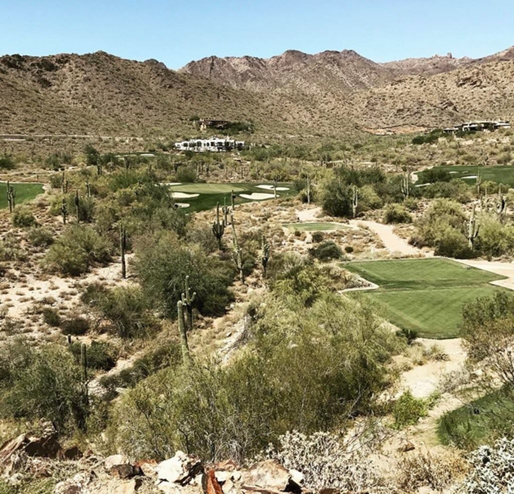 A desert landscape with a golf course, cacti, and mountains in the background.