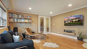 A living room with a sofa, a recliner, a bookshelf, a flat-screen TV, and a sliding glass door leading to a patio.