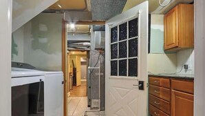 A narrow kitchen with a white door, wooden cabinets, and a tiled floor.