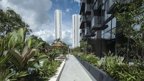 Een pad omzoomd met tropische planten en een modern gebouw met balkons.