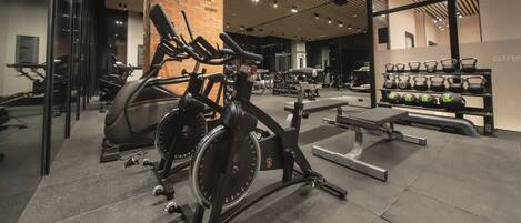 Ein Fitnessstudio mit stationären Fahrrädern, Kraftgeräten und einer Bank.