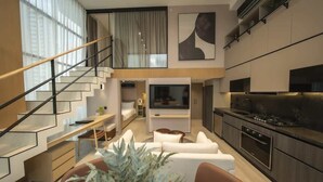 Een modern interieur met een trap, een zithoek met een bank en salontafel, een keuken met fornuis en een grote televisie.