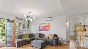 Una sala moderna con un sofá seccional gris, una mesita redonda, una lámpara de pie y un cuadro con una puesta de sol sobre un muelle.