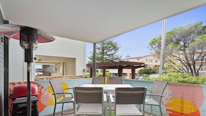 Un patio exterior con mesa y sillas, una parrilla y una pérgola.