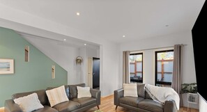A modern living room with two leather sofas, a staircase, and large windows with curtains. - Spacious Townhouse Near Shops and Beach (Cowes)