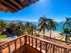 Ein Balkon mit Blick auf einen Strand, Palmen und ein Schwimmbecken.
