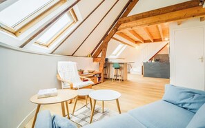 Ein Loft-Zimmer mit schrägem Dach, Oberlichtern, einer Couch, einem kleinen Tisch und einem Stuhl.